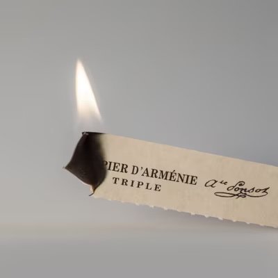 Papier d'Arménie incense burning paper strip smoldering on heat-safe dish – French home fragrance ritual